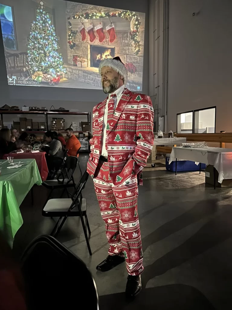 A person in a festive suit and Santa hat stands in a decorated room with a projected Christmas scene in the background, reflecting the seamless shipping logistics behind holiday cheer.