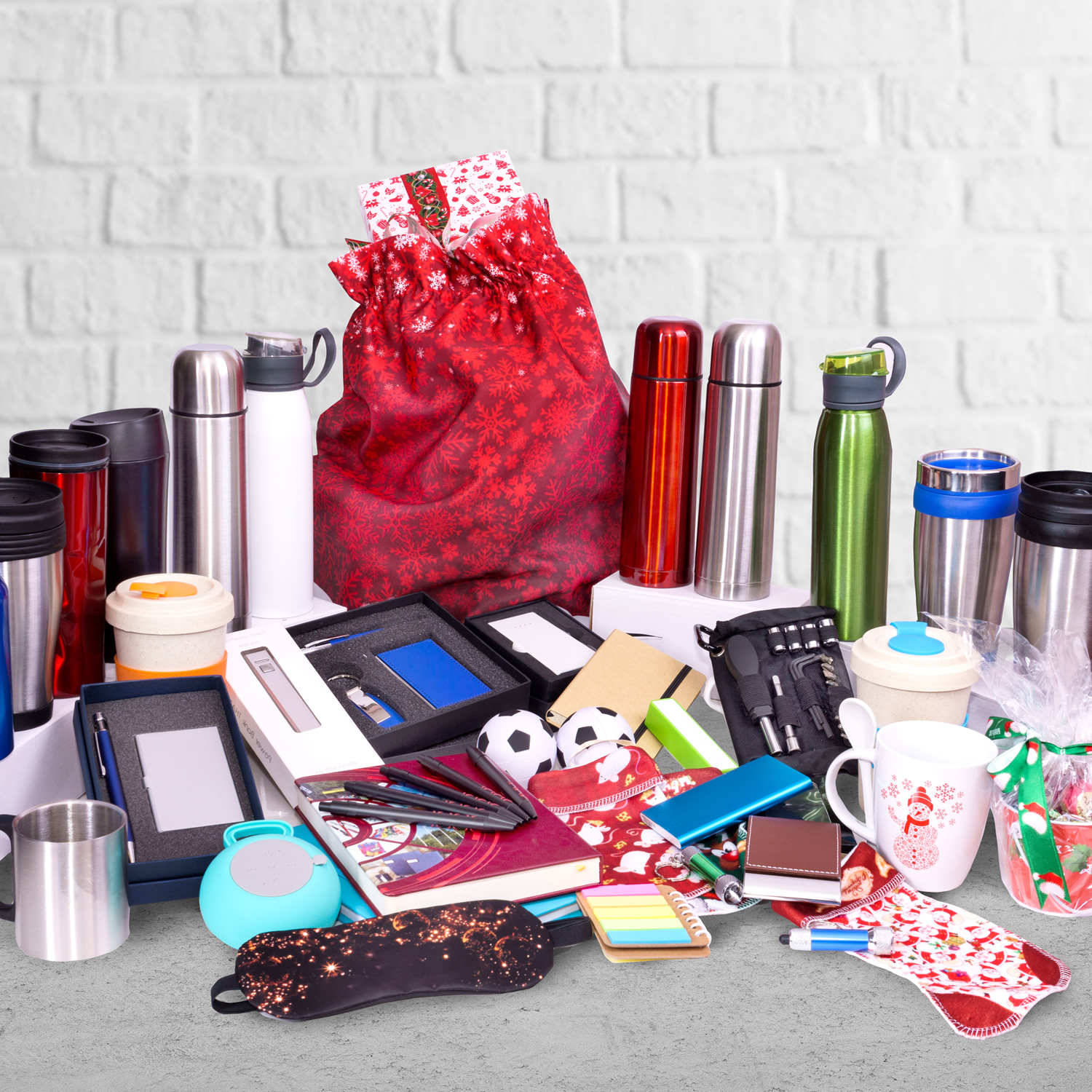 A collection of various items including thermoses, notebooks, pens, water bottles, soccer balls, toolkits, and gift bags displayed against a white brick background highlights the seamless logistics needed for warehouse fulfillment.