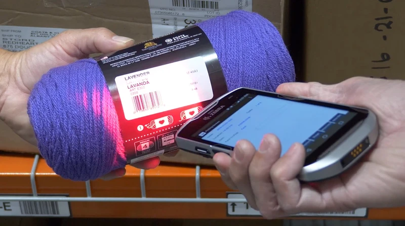 A person in the warehouse scans a purple yarn label with a handheld barcode scanner, ensuring seamless fulfillment.