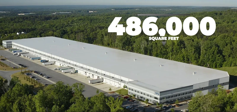 Aerial view of a sprawling logistics warehouse building surrounded by trees, with "486,000 square feet" text displayed in the sky above the warehouse.