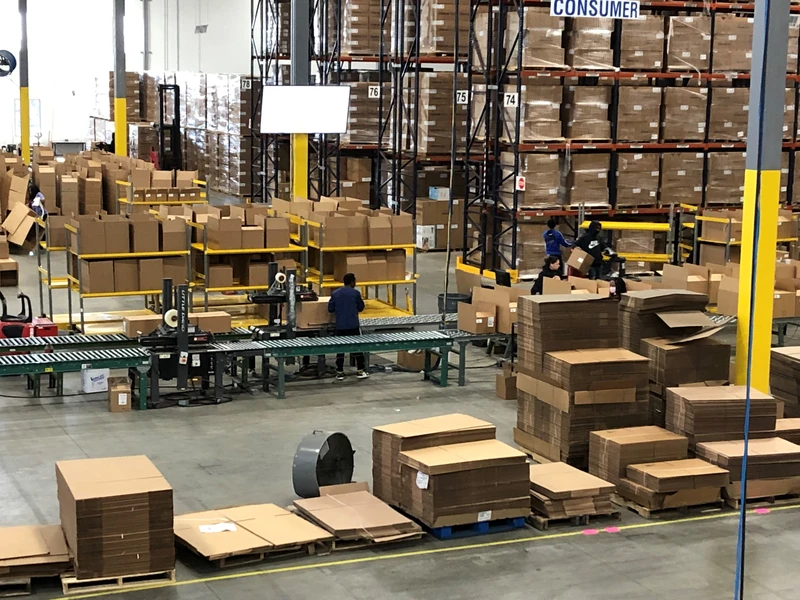 A busy warehouse with employees handling packages on conveyor belts and picking items for orders, showcasing a well-structured storage system and fulfillment operations in progress.